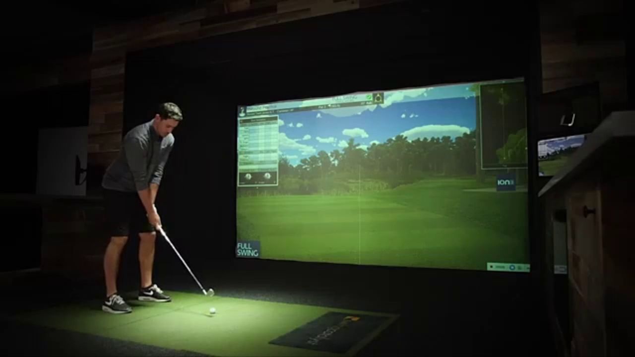 A golfer lining up a shot in a simulator bay
